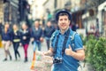 Traveler with trendy look holding map showing thumb up on street full of restaurants and shops of european city